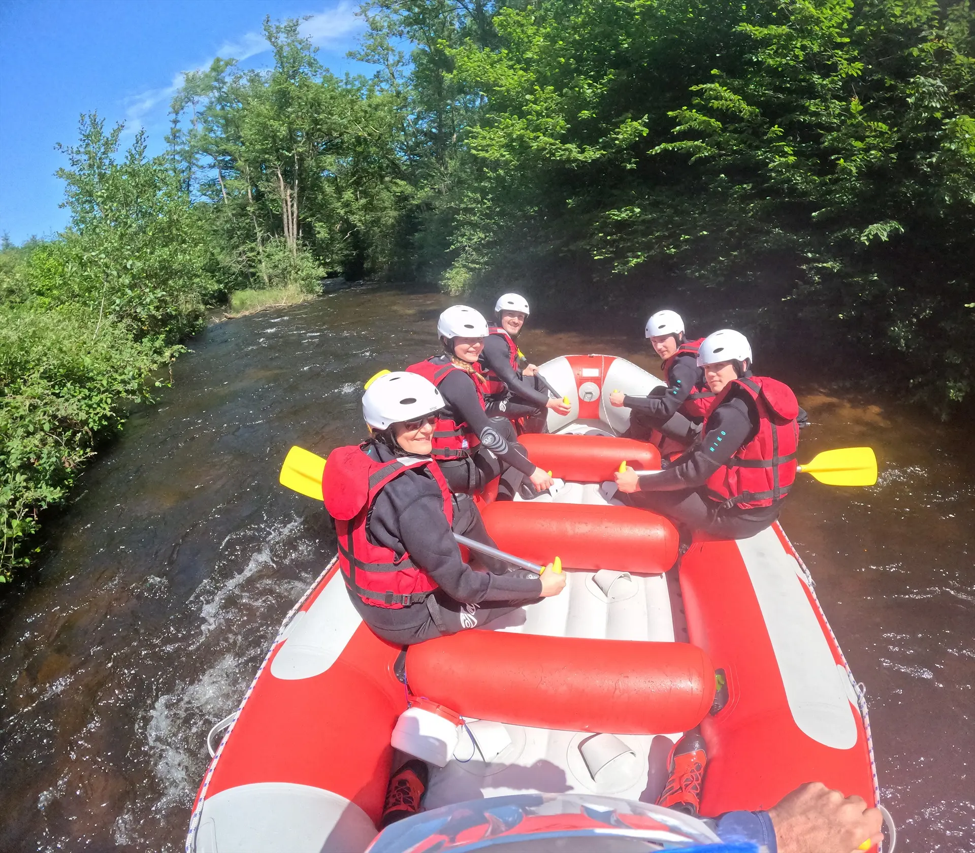 Groupe souriant en casques blancs et gilets rouges à bord d’un raft sur le Chalaux, entre les berges boisées du Morvan.