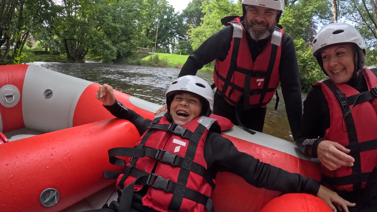 Enfant riant, adossé au boudin d’un raft rouge, avec deux autres participants sur le Chalaux, dans le Morvan.