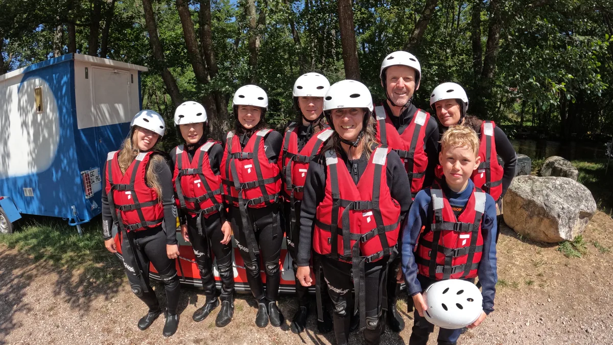 Groupe d’adultes et d’enfants en combinaisons et gilets rouges posant à terre lors d’une sortie rafting dans le Morvan.