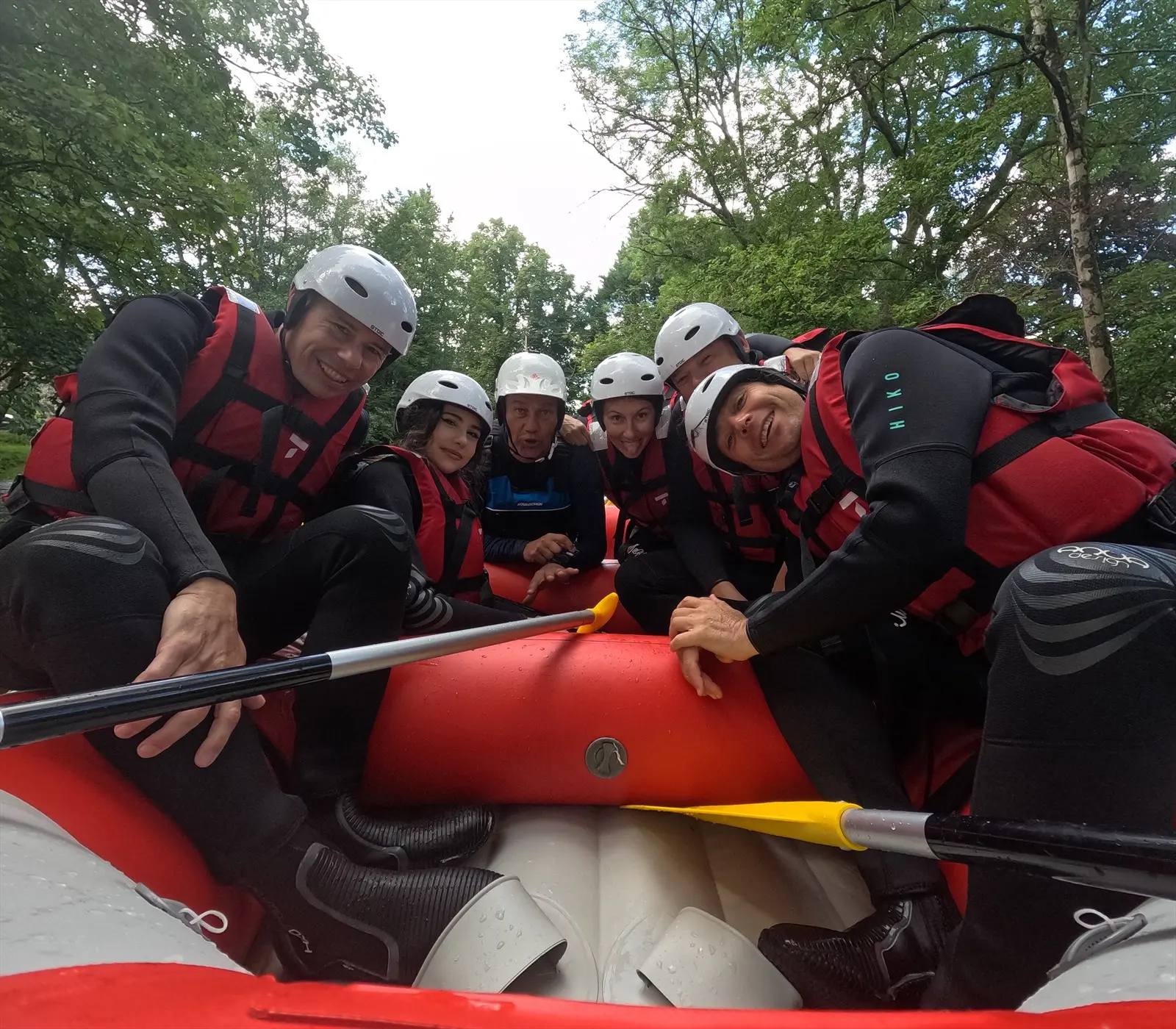 Groupe souriant penché vers la caméra à bord d’un raft rouge, avec le guide en gilet bleu, sur le Chalaux dans le Morvan.