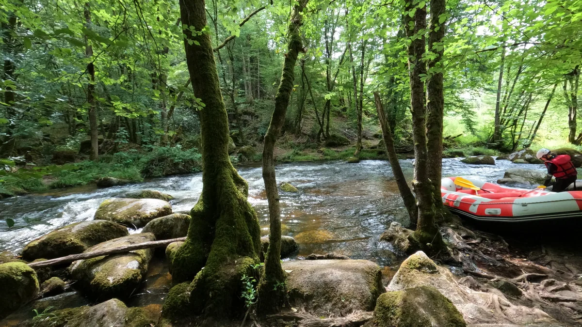 Raft rouge sur le Chalaux derrière des arbres et des rochers moussus du Morvan.